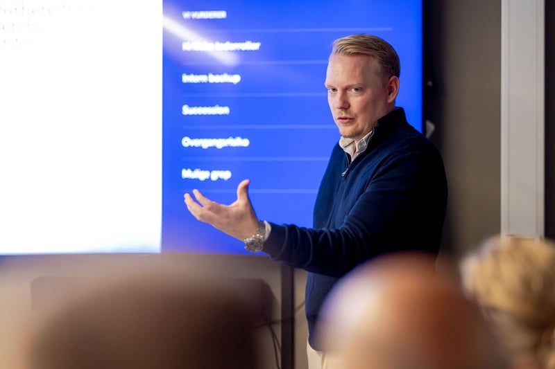 A man presenting in front of a screen and explaining with an open hand