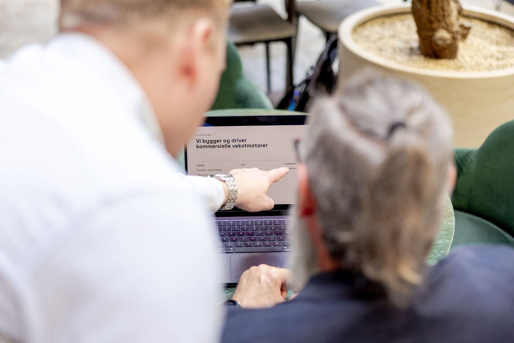 Two colleagues at a laptop, one pointing at a web page on the screen